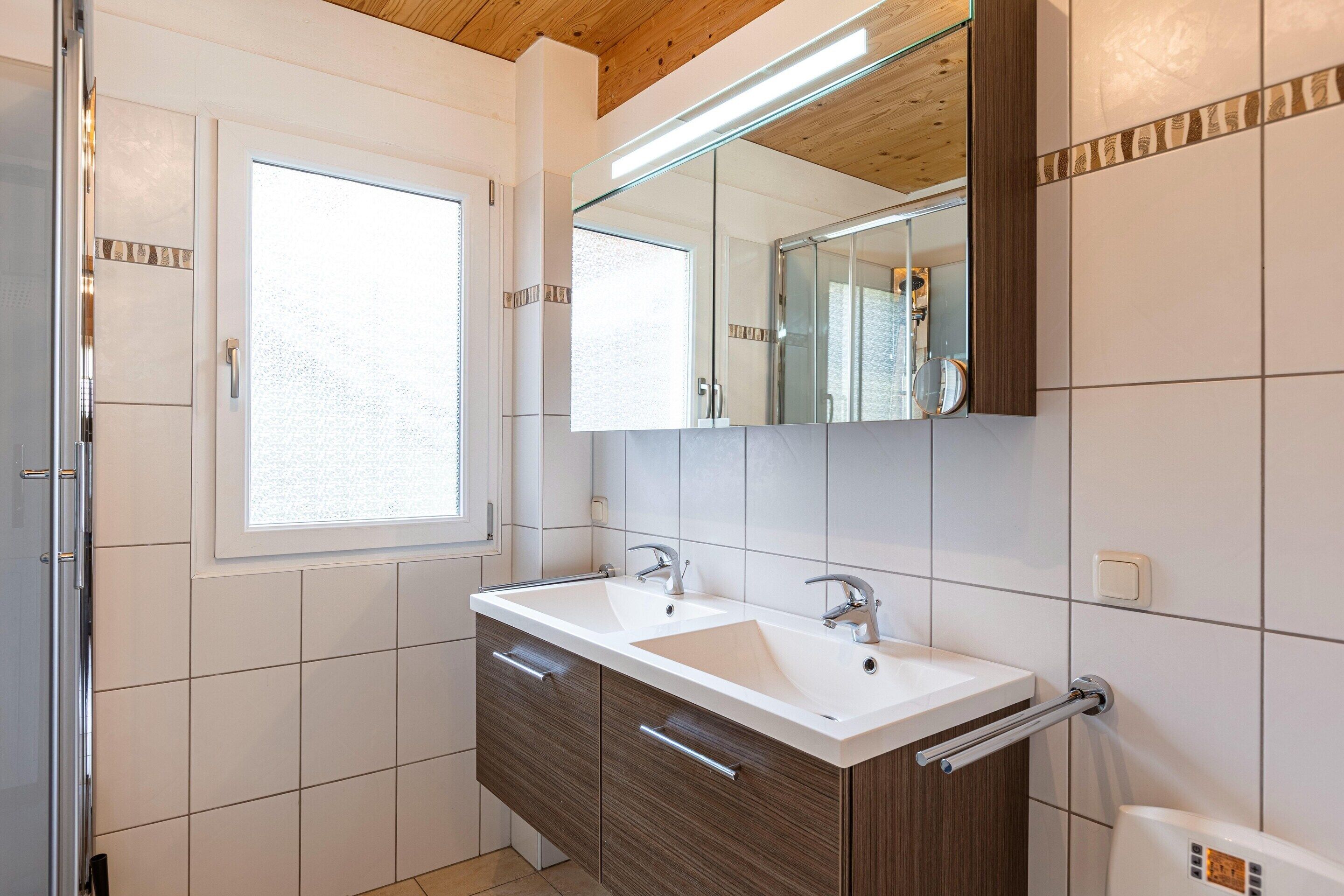 Ein Badezimmer mit einem Doppelwaschbecken, Holzschränken, einem großen Spiegel und einem Fenster.