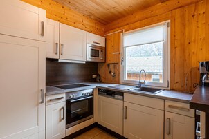 Una cocina moderna con armarios blancos, electrodomésticos de acero inoxidable y una ventana con persianas.
