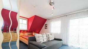 Ein Schlafzimmer mit Bett, Sofa, einem Fenster mit Vorhängen und einer Deckenleuchte.