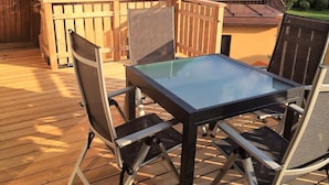 Eine Holzterrasse mit einem Glastisch und Metallstühlen.