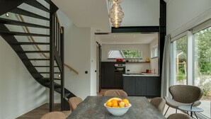 A modern kitchen with dark cabinetry, a built-in oven, and a window overlooking a garden. - Bungalow in Texel Near National Park (De Koog)