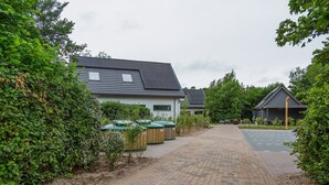 A paved pathway leading to a building with a sloped roof, surrounded by greenery and equipped with outdoor waste bins. - Bungalow in Texel Near National Park (De Koog)
