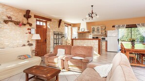 A living room with a sofa, armchair, and coffee table, a kitchen with a dining table, and a stone wall. - Cosy Holiday Home Near the Causses du Quercy (Lavercantiere)