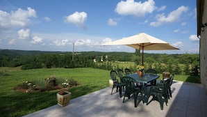 An outdoor patio with a table and chairs, a large umbrella, and a view of a green landscape. - Cosy Holiday Home Near the Causses du Quercy (Lavercantiere)