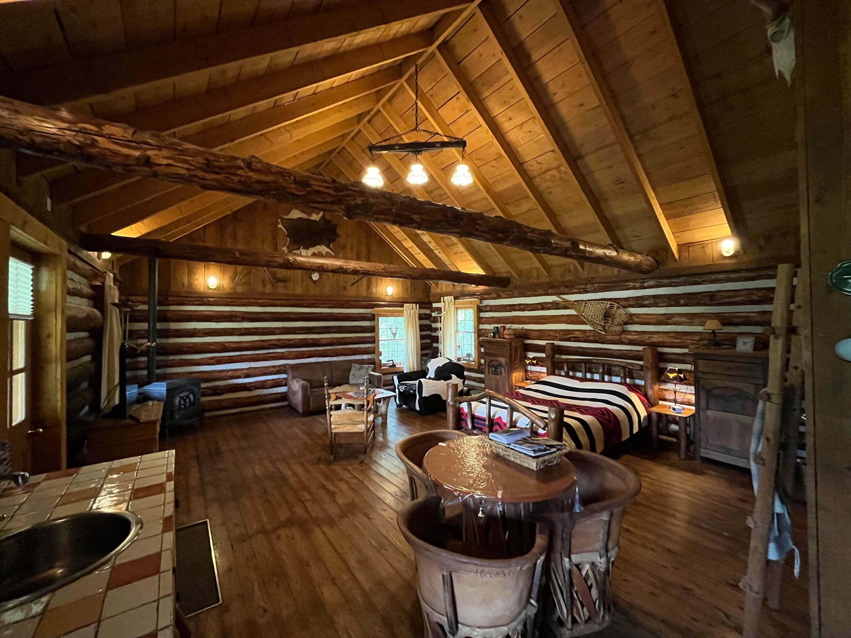 A log cabin interior with a wooden floor, a dining table, a sofa, and a fireplace.