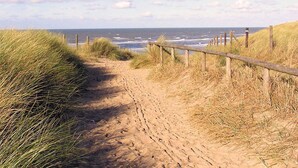 En sandstig som leder ner till stranden, med ett trästaket och gräs på vardera sidan.