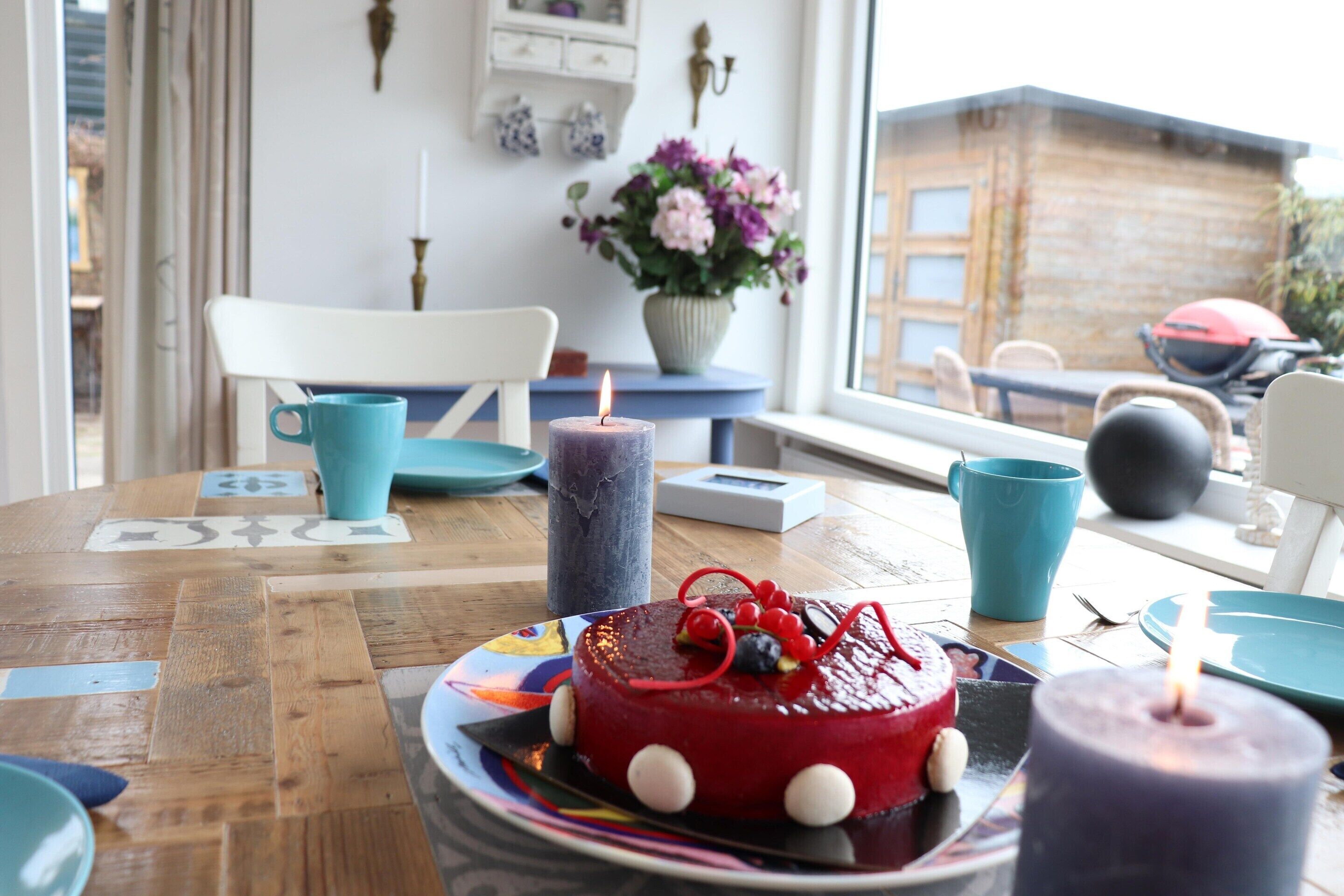 A dining table with a cake, candles, and a vase of flowers.