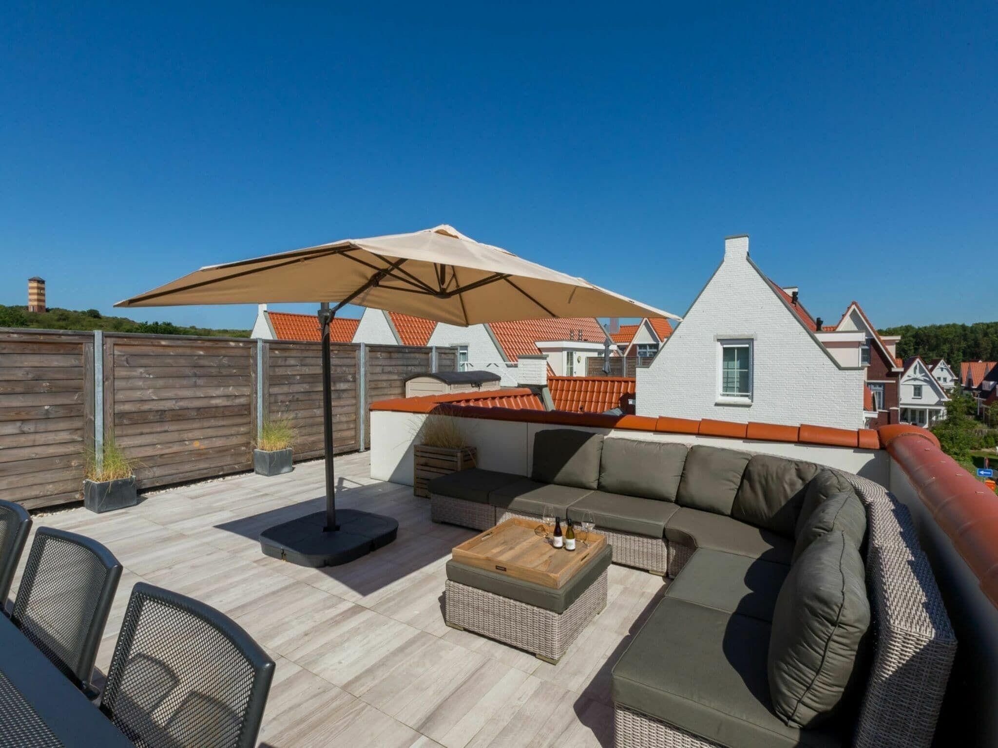 Une terrasse sur le toit, aménagée avec du mobilier d’extérieur, notamment un canapé et des fauteuils, ainsi que deux parasols pour créer de l’ombre.