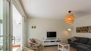 A modern living room with a TV, wicker chairs, a sofa, and a balcony with glass doors. - Luxurious Apartment in Koudekerke With Parking (Koudekerke)