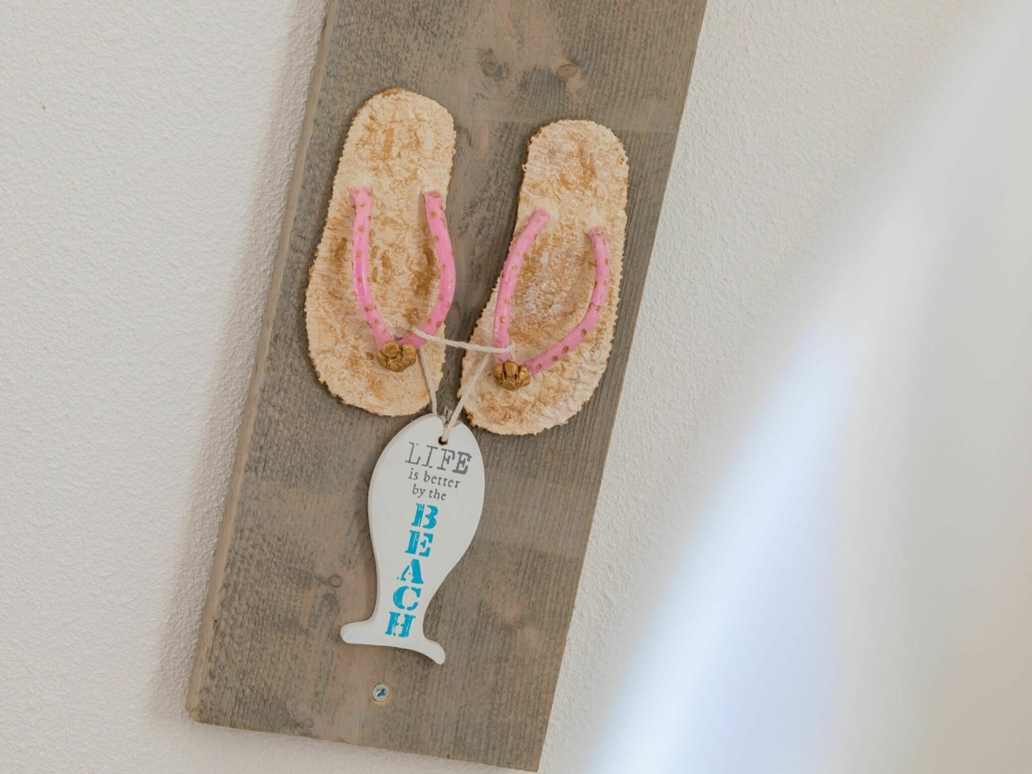 A pair of flip-flops hanging on a wooden board with a tag that reads "LIFE is better by the BEACH."