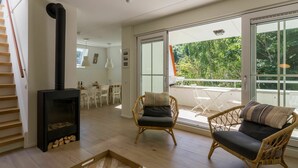 A modern living room with a fireplace, wicker chairs, a dining area, and a balcony with a view of greenery. - Luxurious Apartment in Koudekerke With Parking (Koudekerke)
