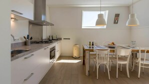 A modern kitchen with white cabinetry, a gas stove, and a dining area with white chairs and a wooden table. - Luxurious Apartment in Koudekerke With Parking (Koudekerke)