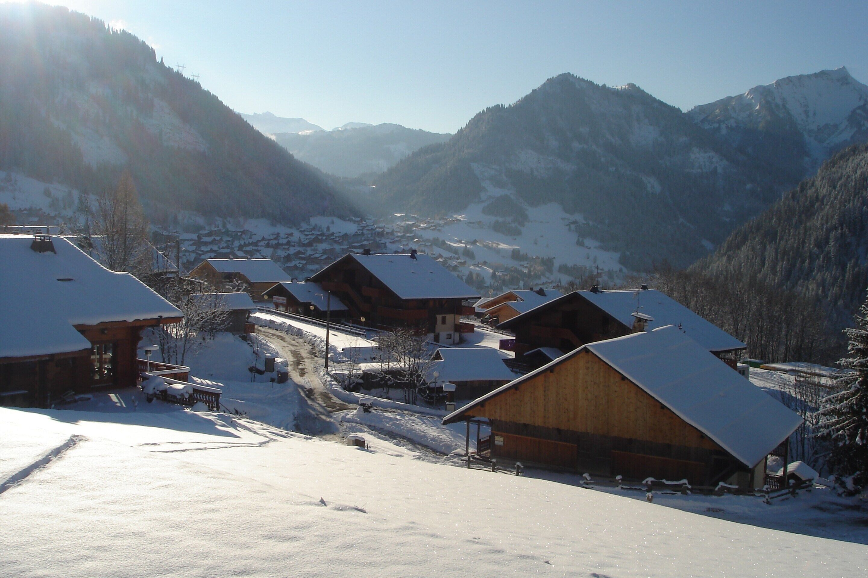 A snow-covered village with wooden buildings, a clear sky, and mountains in the background.