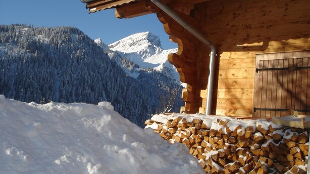 Een houten hut met een met sneeuw bedekte dak, een houten deur en uitzicht op een besneeuwde berg.