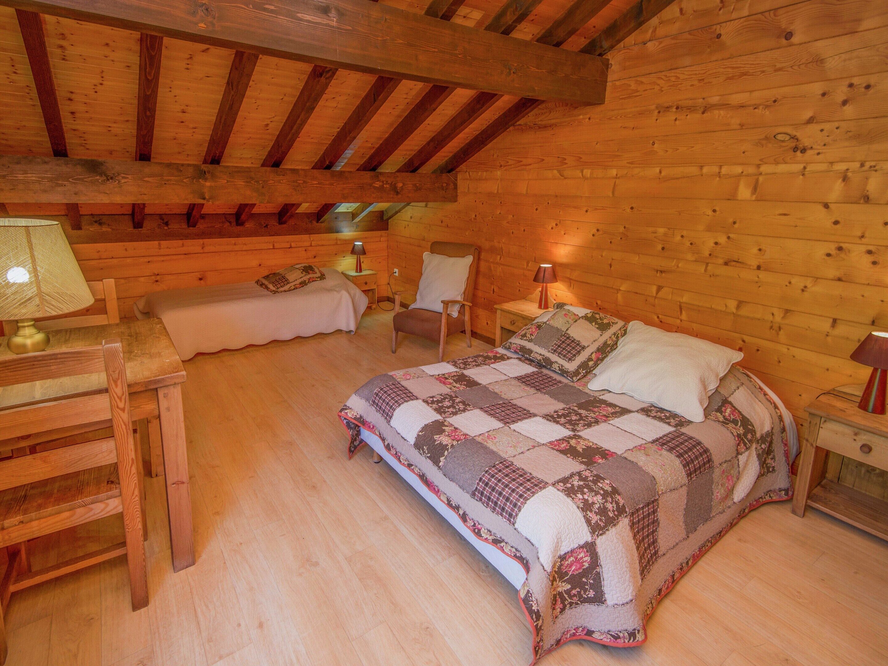 Ein gemütliches Schlafzimmer in einer Blockhütte mit einem Bett, zwei Nachttischen, einem Sessel und einer Lampe.
