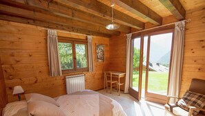 Een slaapkamer in een houten blokhut met een bed, een tafel, een stoel en uitzicht op de natuur.