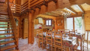 Een houten chalet van binnen met een eethoek, keuken en een trap.