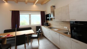 A modern kitchen with wooden beams, a dining area with a table and chairs, and a window with curtains. - Luxurious Apartment in Fugenberg With Balcony (Fuegenberg)