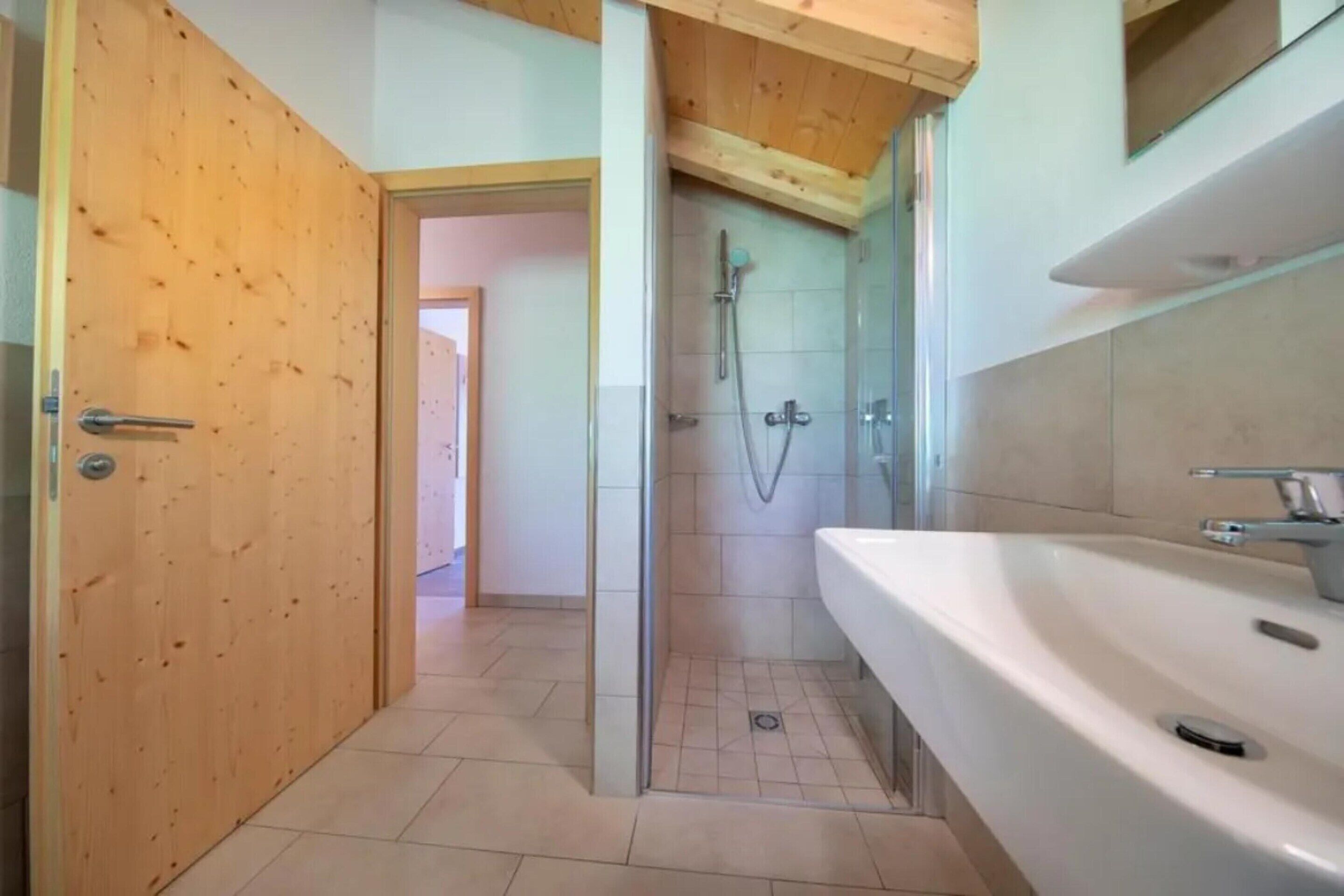 A bathroom with a wooden door, a shower, and a white sink.