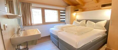 A bedroom with a bed, a bedside table, a mirror, a window, and a sink.