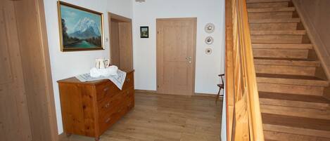 A wooden staircase leading to an upper floor, a wooden dresser with a painting, and a door with decorative plates.