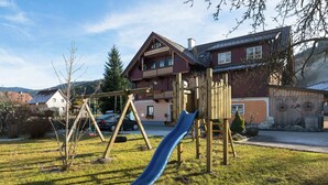 Un parque infantil con tobogán y columpios frente a una casa con balcón.