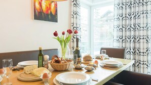 A dining table set with plates, glasses, a bottle, a basket of bread, and a vase with flowers. - Apartment in Leogang Near Ski Slopes (Leogang)