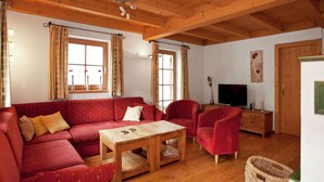 Un accogliente soggiorno con un divano rosso, un tavolino in legno e poltrone. C'è una televisione su un mobile in legno e una finestra con tende.