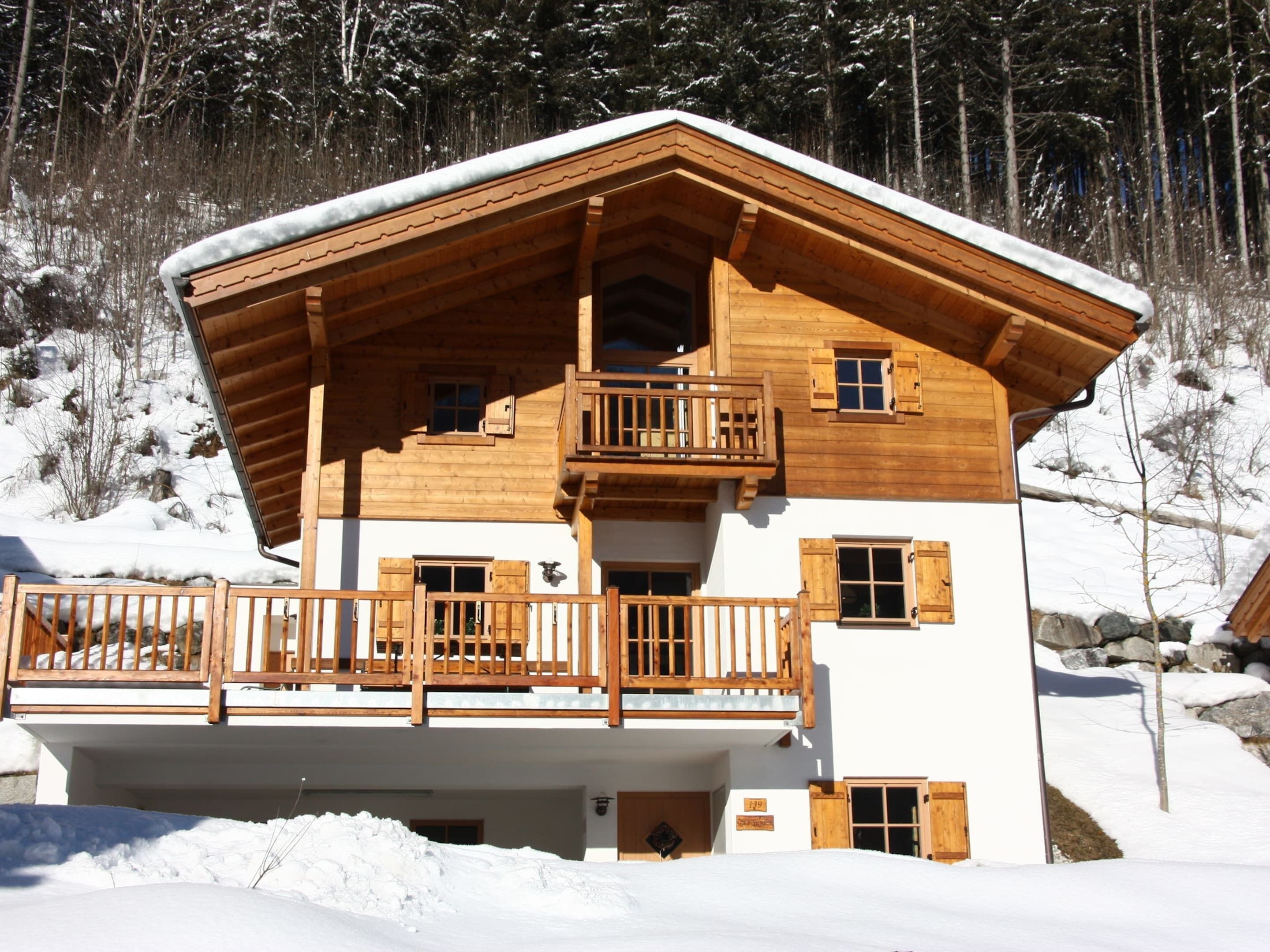A wooden chalet with a balcony, set in a snowy landscape.