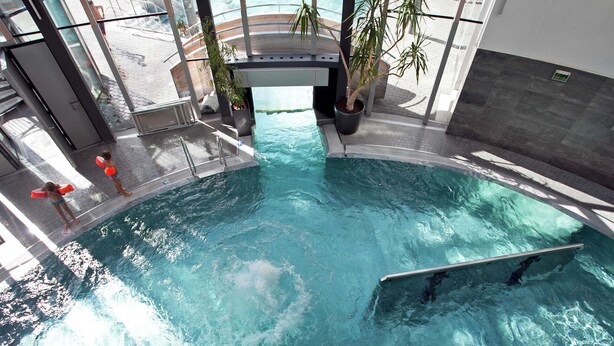 Piscina interna con acqua cristallina, circondata da pareti in vetro e piante in vaso.