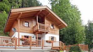 Un chalet in legno a due piani con un balcone, una scala che conduce al piano superiore e un vialetto in pietra.