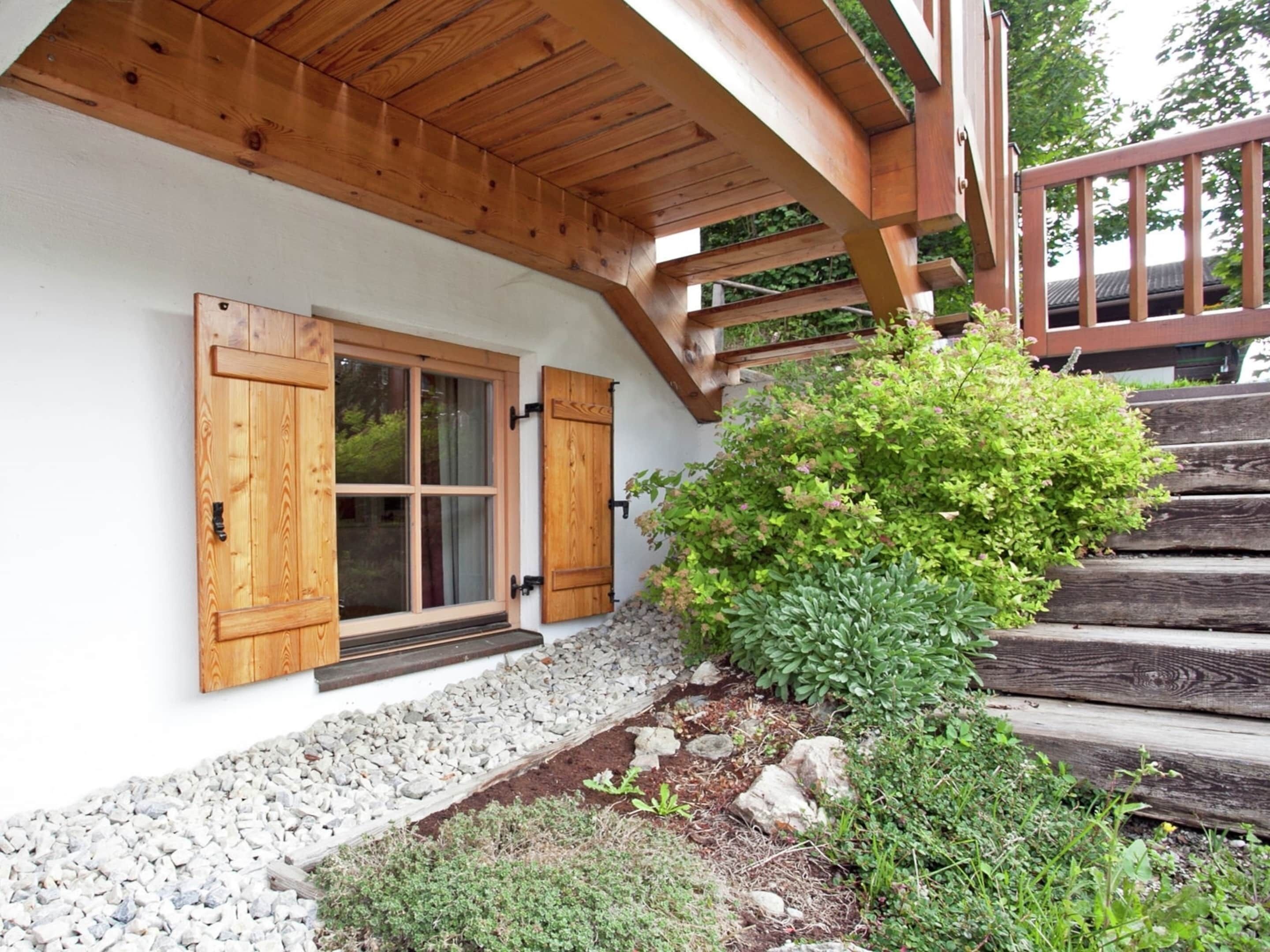 A wooden staircase leading to a white-walled building with a wooden porch and a window with shutters.