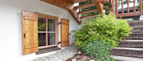 A wooden staircase leading to a white-walled building with a wooden porch and a window with shutters.