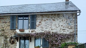 Ein Steinhaus mit Kiesweg, einem schwarzen Tor und einem kleinen Garten mit Stuhl und Blumentöpfen.