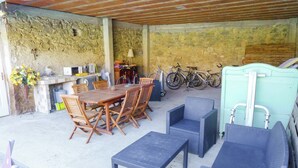 An outdoor patio with a stone wall, a wooden table with chairs, a blue wicker sofa, and bicycles parked against the wall. - Holiday Home Talairan With Pool and BBQ (Talairan)