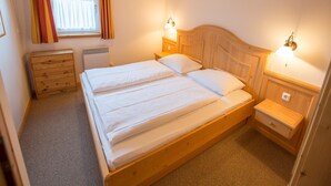 Una cama de madera con dos almohadas en una habitación con techo inclinado y una ventana con cortinas.