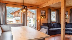 Un interior de madera con una mesa de comedor, sofás y un amplio ventanal que ofrece vistas a una montaña.