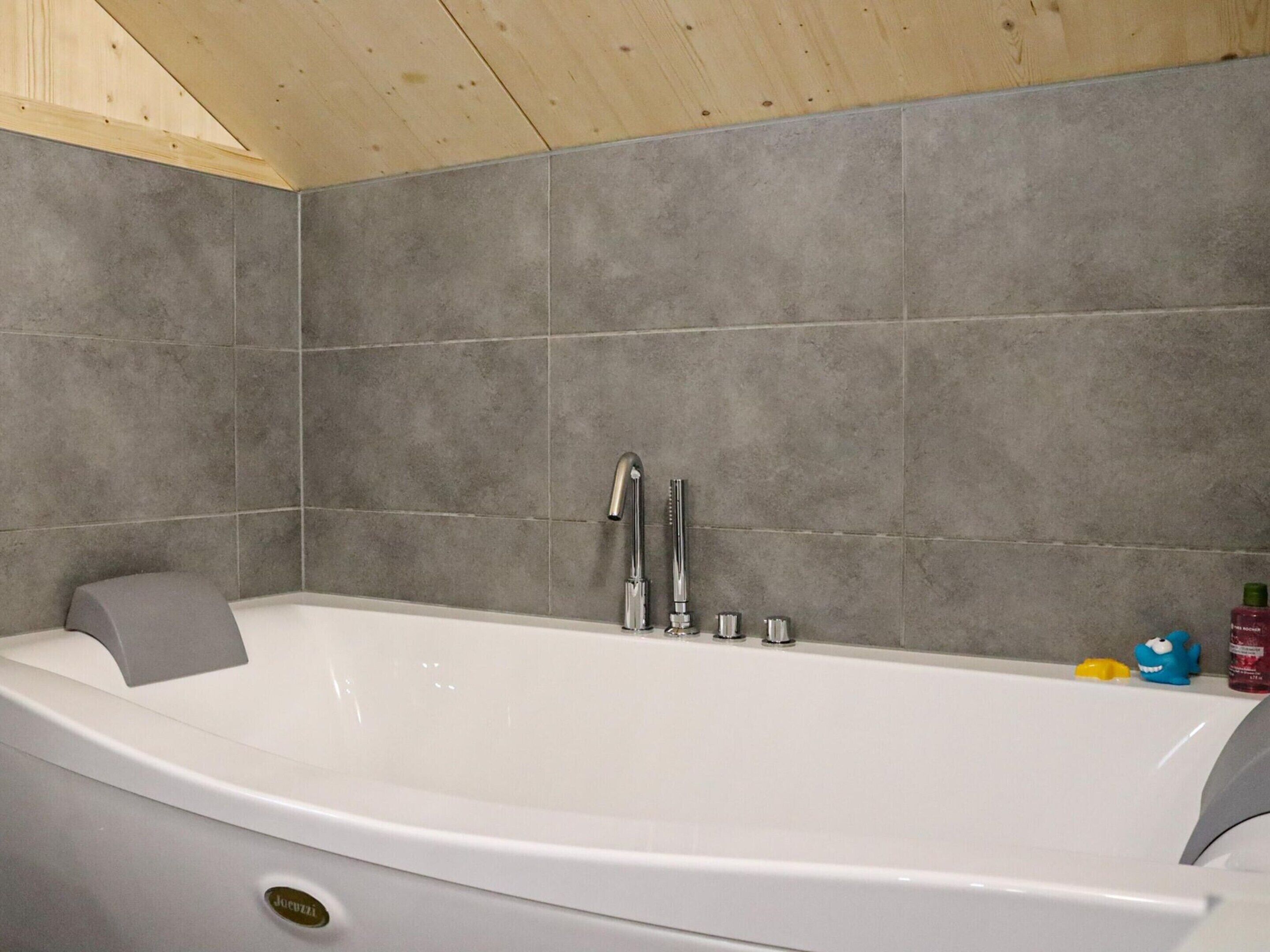 Un baño moderno con una bañera independiente, paredes de azulejos grises y techo de madera.
