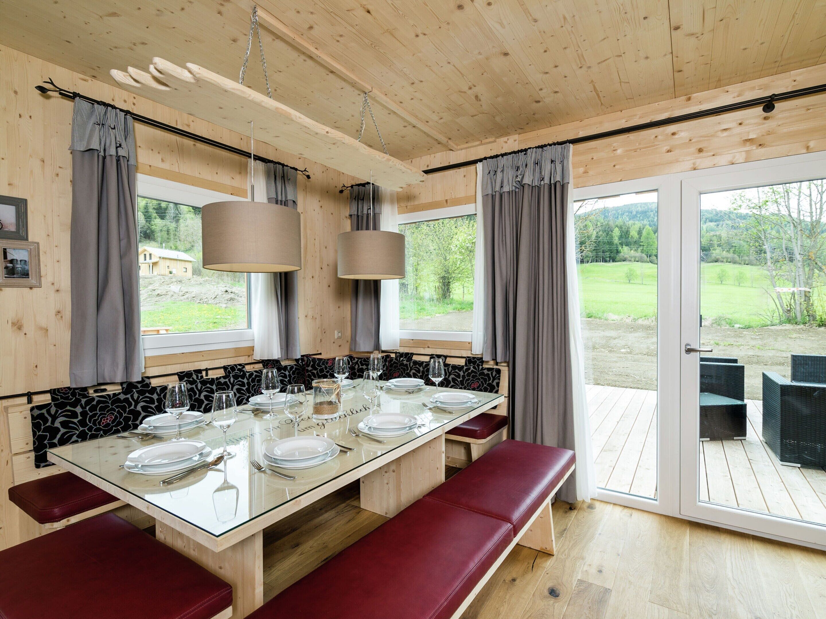 Un comedor con una mesa de vidrio preparada para seis personas, bancos de madera y vistas al exterior.