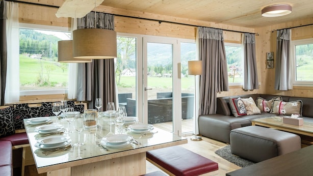 A modern, well-lit dining area with a glass table set for four, surrounded by wooden walls and large windows offering a view of a green landscape. - Luxurious Chalet in Sankt Georgen ob Murau with Hot Tub (Sankt Georgen am Kreischberg)