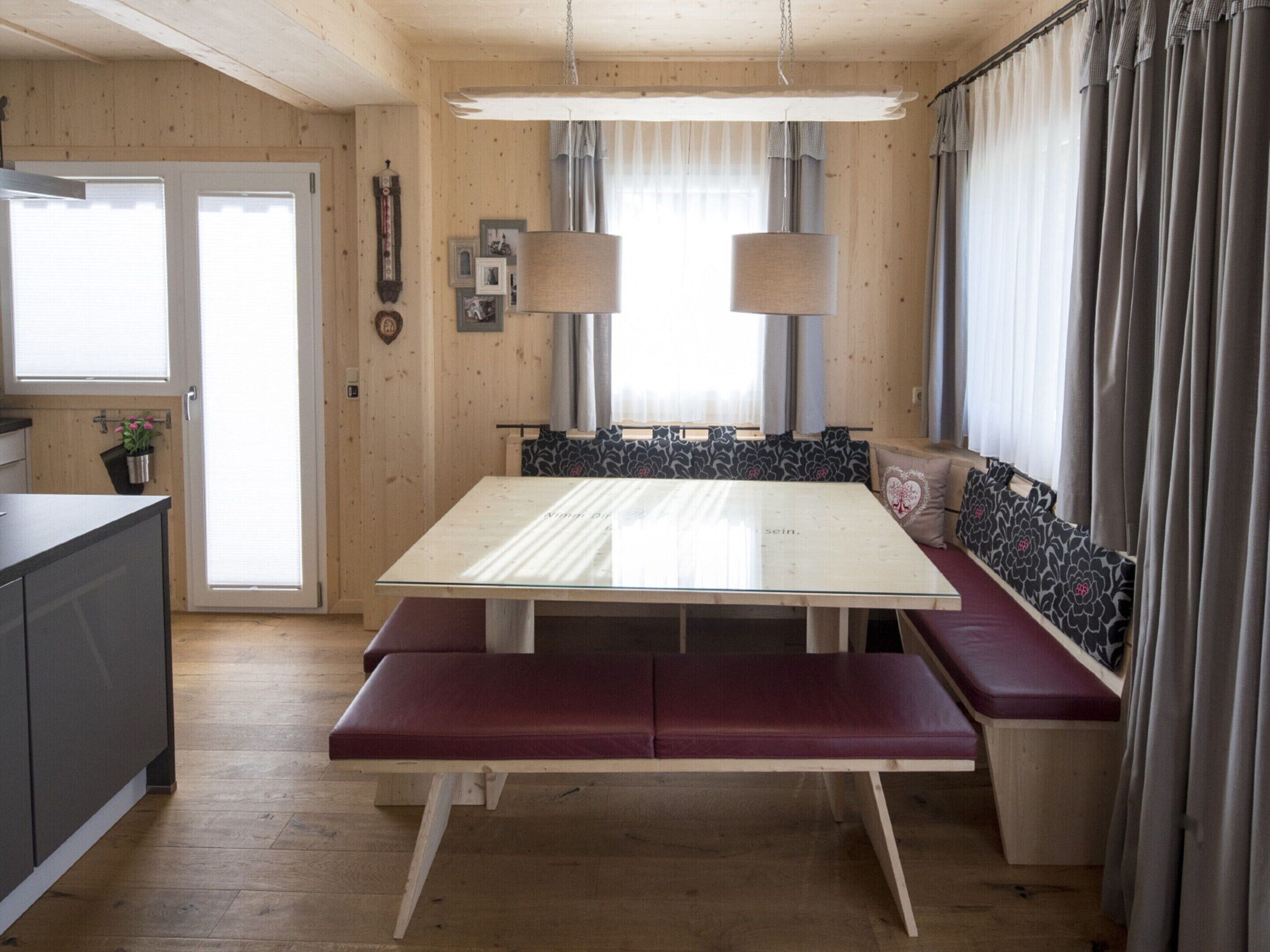A cozy cabin interior with a wooden dining table, bench seating, and a built-in bench along the window.