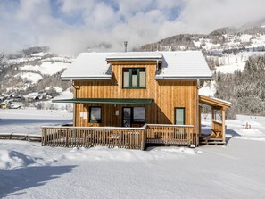 A wooden chalet with a balcony and a covered porch, surrounded by snow-covered mountains. - Luxurious Chalet in Sankt Georgen ob Murau with Hot Tub (Sankt Georgen am Kreischberg)