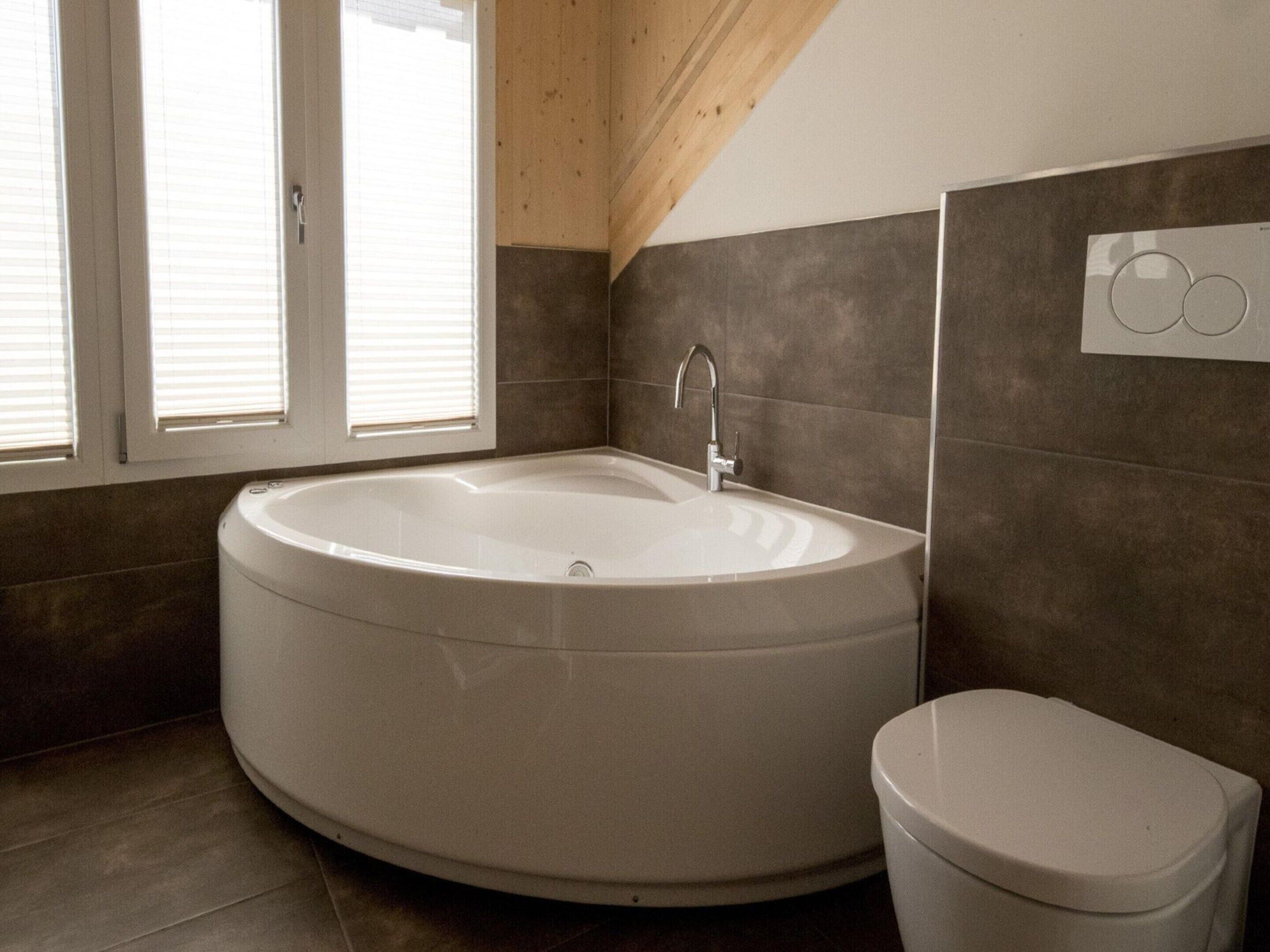 Un bagno moderno con una vasca freestanding, un water e una finestra con persiane.