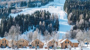 A snow-covered ski resort with wooden cabins and a ski lift. - Luxurious Chalet in Sankt Georgen ob Murau with Hot Tub (Sankt Georgen am Kreischberg)