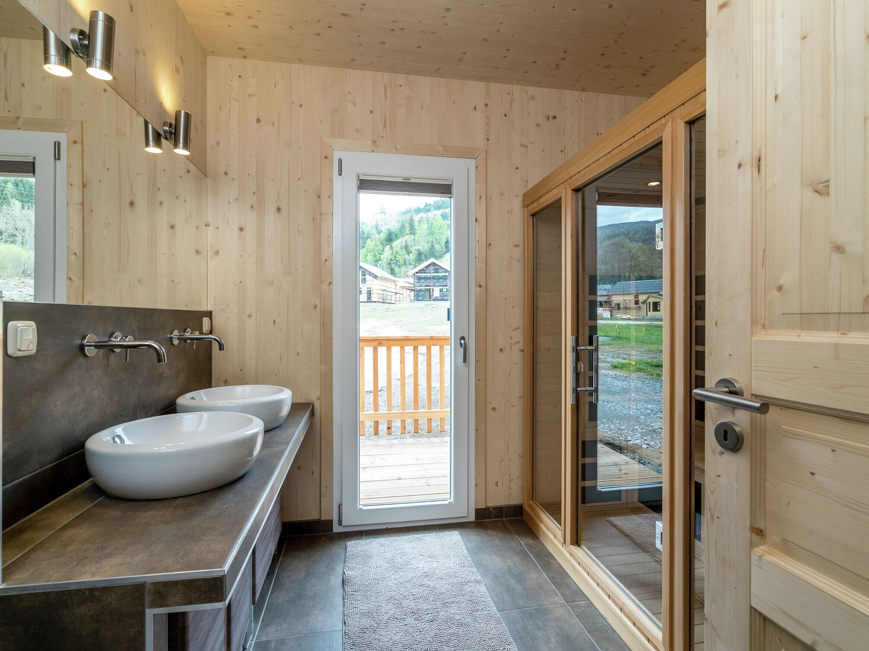 A modern bathroom with two sinks, a mirror, and a wooden door leading to a balcony.