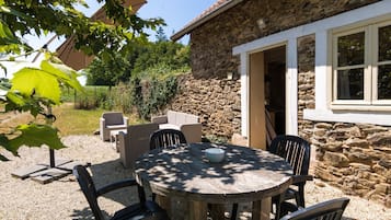 A stone building with a round wooden table and chairs, a stone wall, and a garden area with chairs and a table.