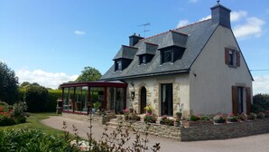 A two-story house with a covered porch, stone foundation, and a garden with flowers. - Peaceful Forest Stay in Pedernec (Pedernec)