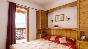 Ein Schlafzimmer mit Holzkopfseitenverkleidung, einem Bett mit rot-weißer Bettwäsche, einem Fenster mit Ausblick und einem Wandregal mit Bild und Lampe.