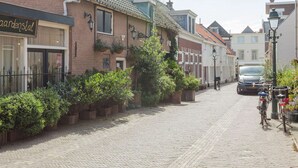 Une rue pavée bordée de bâtiments européens traditionnels, une voiture garée et un vélo.