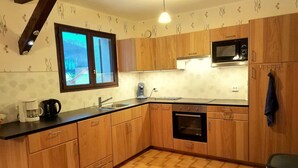 A kitchen with wooden cabinets, a microwave, an oven, a sink, and a window. - Cozy Chalet Escape in the Alps (Saint-Jean-de-Vaulx)